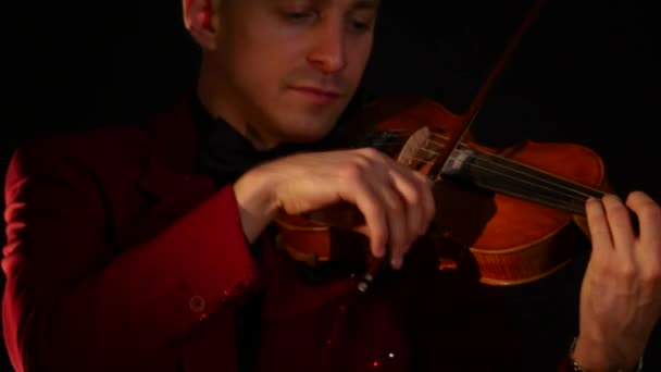 赤いスーツを着た若い男が黒の背景にバイオリンを演奏します。 — ストック動画