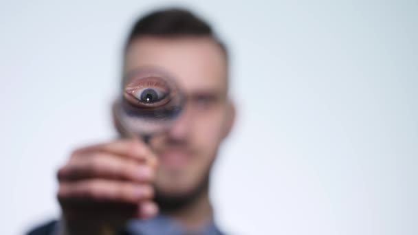 Close up van een geconcentreerde jonge man met behulp van een vergrootglas op witte achtergrond — Stockvideo