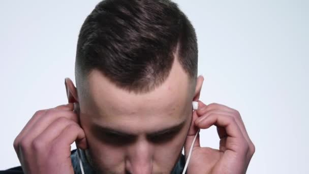 Porträt eines jungen, gut aussehenden Mannes mit Kopfhörern, der isoliert auf weißem Hintergrund Musik auf seinem Handy hört — Stockvideo