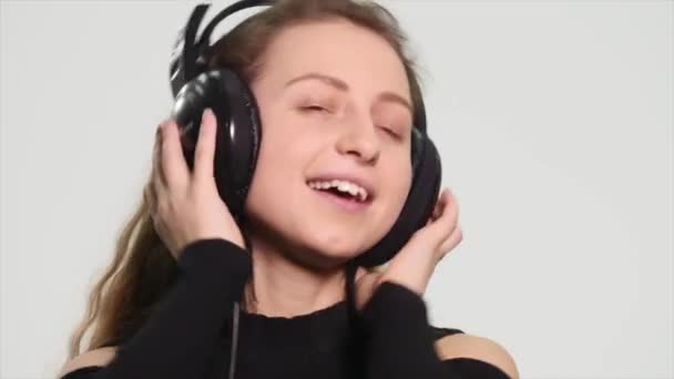 Χορεύουν και τραγουδούν στα ακουστικά σε λευκό φόντο. Όμορφη κοπέλα, ακούγοντας μουσική και το συναισθηματικό τραγούδι σε λευκό φόντο — Αρχείο Βίντεο