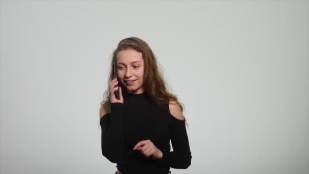 Mujer joven sonriendo y hablando en su teléfono celular sobre un fondo blanco — Vídeo de stock