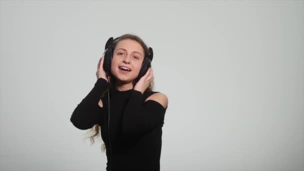 Χορεύουν και τραγουδούν στα ακουστικά σε λευκό φόντο. Όμορφη κοπέλα, ακούγοντας μουσική και το συναισθηματικό τραγούδι σε λευκό φόντο — Αρχείο Βίντεο