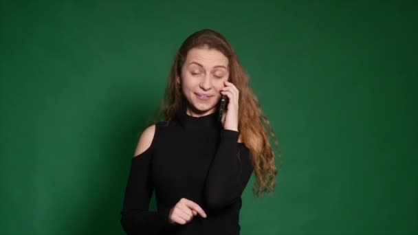 Jonge vrouw glimlachend en praten over haar mobiele telefoon op een witte achtergrond. Vooraanzicht van een casual jongedame spreken op de telefoon en het kijkt weg op groene achtergrond. — Stockvideo