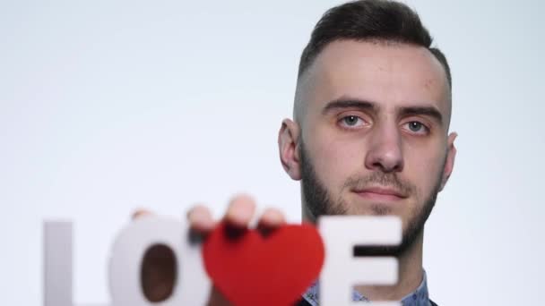 En ung man håller kärlekens inskription på vit bakgrund — Stockvideo