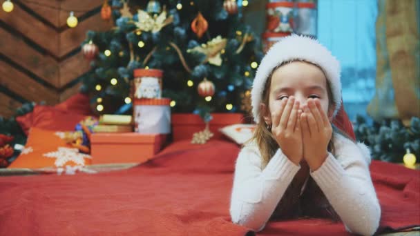 Baby girl send air kiss, spend time near Christmas tree in anticipation of Santa and a gift at Christmas. — Stock video