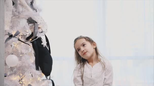 Kleines Mädchen ist total fasziniert von schön geschmücktem Weihnachtsbaum mit Lichtern, Kugeln und Socken. — Stockvideo