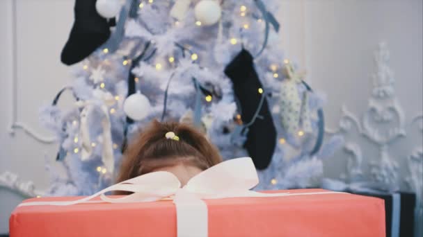 Closeup new year timelapse video of a child appearing from behind the giftbox with her mouth widely opened, rubbing her hands, ready to open the present. — Stock Video