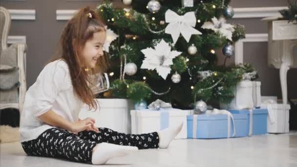 Schattig klein meisje dat met iemand speelt, ze duwt een geschenkdoos en het komt terug naar haar, schuift op de vloer, dan maakt ze een split oefening. — Stockvideo