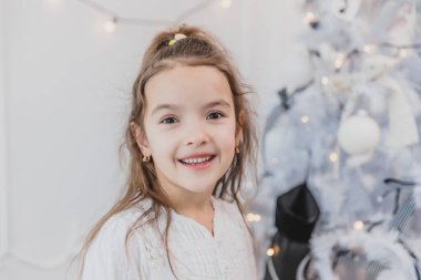 Gülümseyen kız, küçük kar prensesi, Noel ağacının yanında, beyaz bir arka planda..