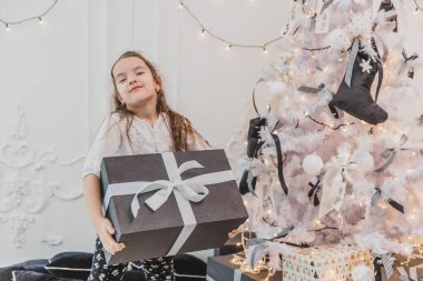 Güzel çocuk Noel 'de en büyük hediyeyi aldığı için mutlu ve şaşırmış ve şimdi de yanında beyaz yay taşıyan bu ağır kutuyu taşıyor..