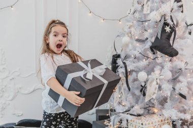 Güzel çocuk Noel 'de en büyük hediyeyi aldığı için mutlu ve şaşırmış ve şimdi de yanında beyaz yay taşıyan bu ağır kutuyu taşıyor..