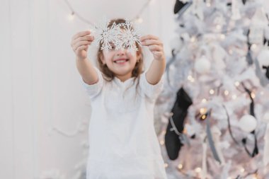 Küçük esmer kız evde bir Noel ağacını gümüş kar flütü ile süslüyor. Ön taraftaki süslemelere odaklan..