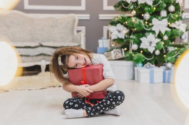 Tam vücut, ön cephede elinde Noel hediyesiyle loto pozisyonunda oturan sevimli bir çocuğun bulanık fotoğrafı, içinde ne olduğunu bulmak..