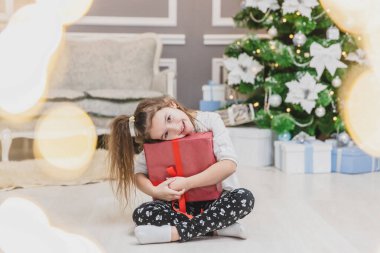 Elinde hediyeyle oturan sevimli bir çocuğun açık renkli fotoğrafı. Noel süslemeli küçük bir cüce gibi..