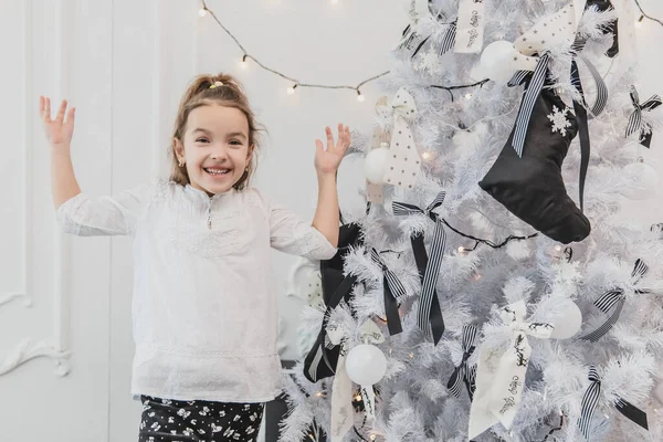 Bambina è totalmente affascinato da albero di Natale splendidamente decorato con luci, palle e calzini . — Foto Stock