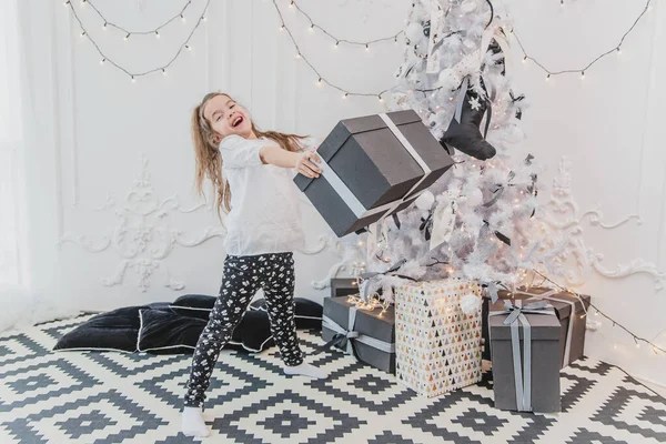 예쁜 아이는 행복해 하고 놀랍니다 크리스마스 선물로 가장 큰 선물을 받았는데 지금은 하얀 활이 달린 무거운 상자를 들고 있어요. — 스톡 사진