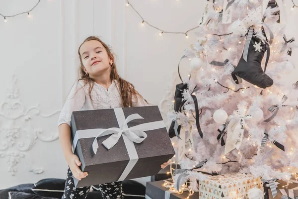 Bella ragazza è felice e sorpreso di ottenere il regalo più grande per Natale e ora lei sta portando questa pesante scatola con fiocco bianco . — Foto Stock