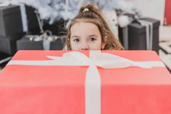 Primer plano foto de año nuevo de un niño mirando desde detrás de la caja de regalo con los ojos abiertos en asombro . — Foto de Stock