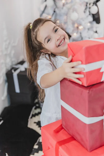 Niedliches Kind bereitete einen Stapel roter Geschenkboxen mit weißen Bändern für ihre Freunde und Familie vor. — Stockfoto