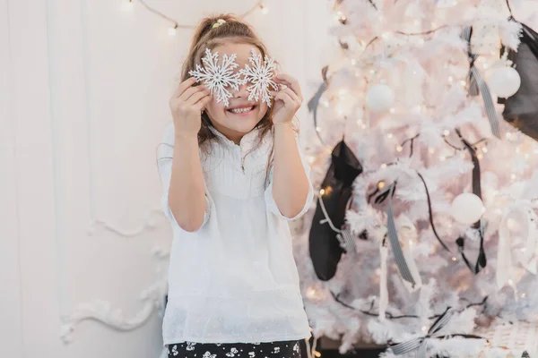 Bambina che gioca con i fiocchi di neve dell'albero di Natale, nascondendo i suoi occhi dietro di loro . — Foto Stock