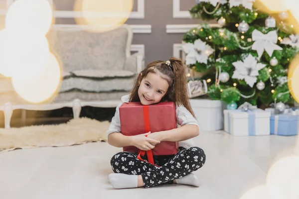 Full-body, foto sfocata in prima linea di bambino carino seduto in posizione foto con un regalo di Natale in mano, scoprire cosa c'è dentro . — Foto Stock