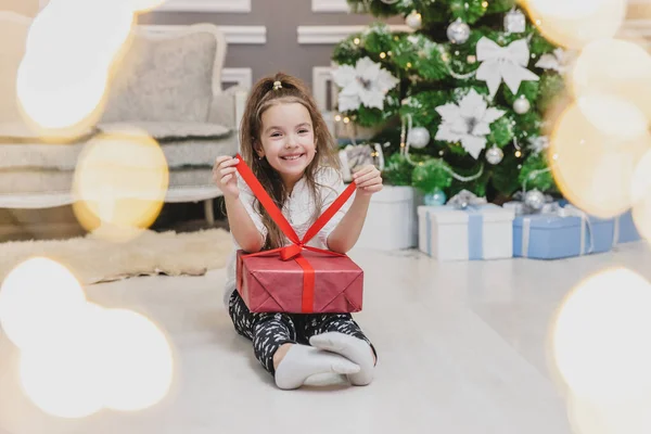 Ganzkörper, vorne verschwommenes Foto eines niedlichen Kindes in Lotos-Position mit einem Weihnachtsgeschenk in den Händen, das herausfindet, was drin ist. — Stockfoto