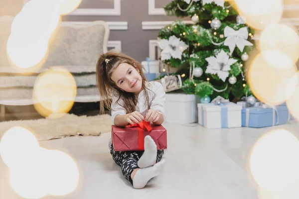 Photo légère de mignon enfant assis avec un cadeau dans les mains, comme un petit gnome dans la chambre décorée de Noël . — Photo