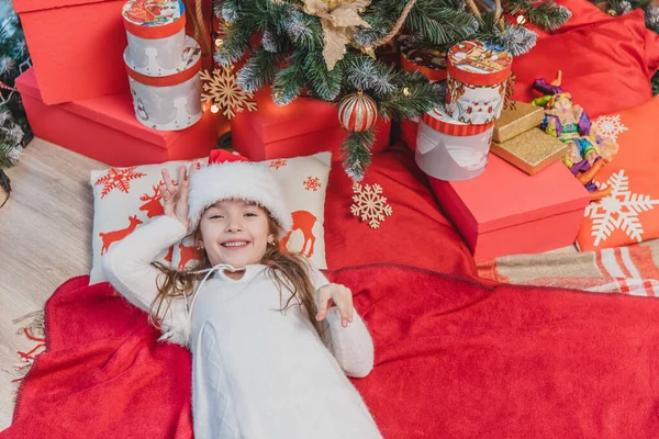 Père Noël enfant couché sur l'oreiller avec impression de renne et couverture rouge sous l'arbre de Noël . — Photo