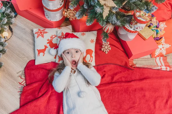 Père Noël enfant couché sur l'oreiller avec impression de renne et couverture rouge sous l'arbre de Noël . — Photo