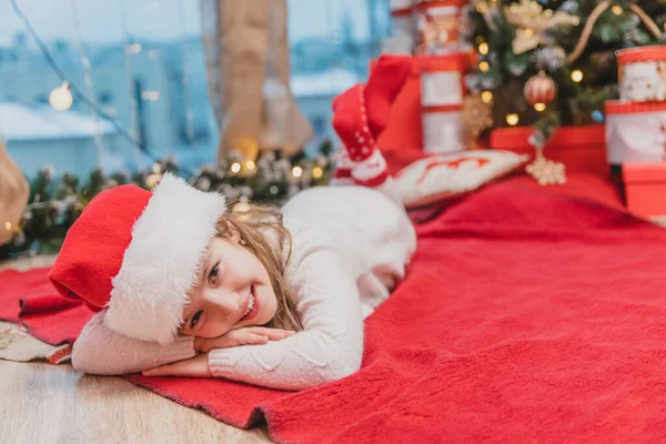 Santa claus kid laying on the red blanket under Christmas tree. — Stock Photo, Image
