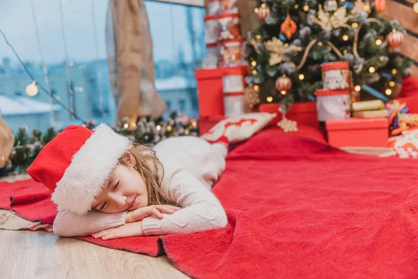 Angelico bambino figlia sta dormendo sulla coperta rossa vicino all'albero di Natale con regali . — Foto Stock