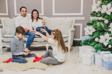 Küçük bir çocuk ve kız elleriyle kar taneleri büyülüyorlar, ebeveynler onlara bakarken, kanepede otururken..