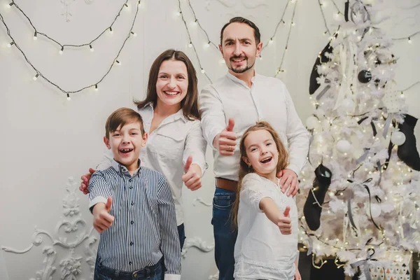 Los padres cariñosos y los niños pequeños quieren tener una foto cerca del árbol de Navidad, están posando y dando pulgares arriba . — Foto de Stock