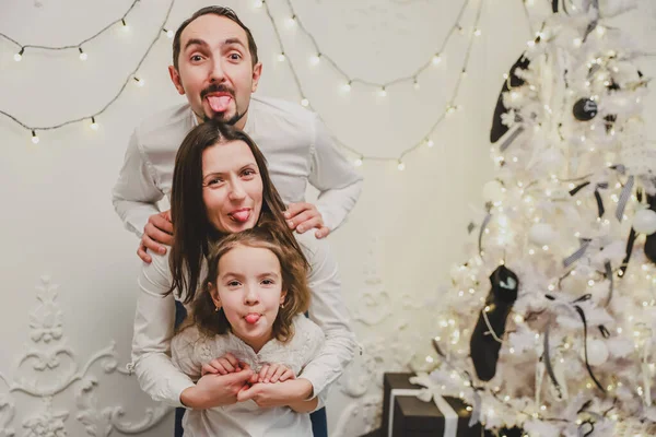 Niedliche Familie spielt am Weihnachtsmorgen herum, lustige Vater Mutter und Tochter bleiben in der Position, wo ihre Köpfe übereinander liegen und zeigen Zungen. — Stockfoto