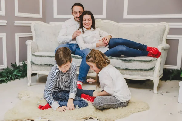 Foto de papá, mamá y su hija en casa cerca del árbol de Navidad, todos sonríen. Los niños juegan en la vanguardia . — Foto de Stock