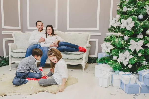 Foto de papá, mamá y su hija en casa cerca del árbol de Navidad, todos sonríen. Los niños juegan en la vanguardia . —  Fotos de Stock