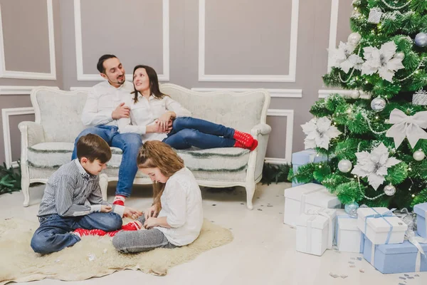 Foto de papá, mamá y su hija en casa cerca del árbol de Navidad, todos sonríen. Los niños juegan en la vanguardia . — Foto de Stock