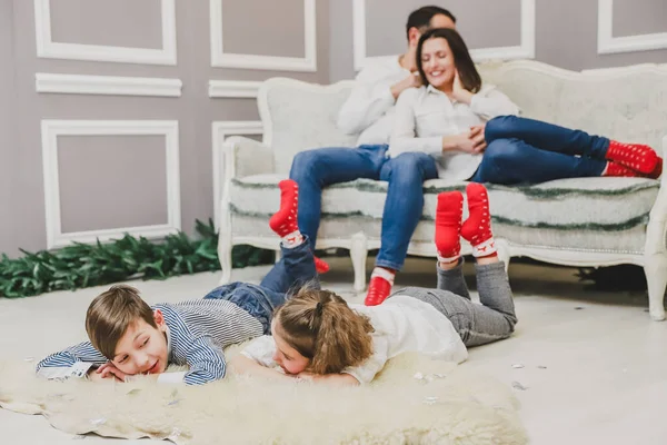 Los miembros adorables de la familia en los calcetines rojos se reúnen del nuevo año. Niños soñolientos están tendidos en la alfombra blanca . — Foto de Stock
