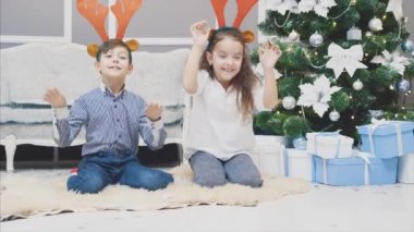 Noel geyiği boynuzu takan, önünde eğilen, gülümseyen ve komik görünen kardeşlerin komik videosu..