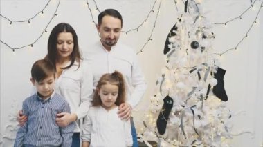 Mutlu aile üyeleri: anne, baba, oğul, kız beyaz arka planda Noel ağacı yakınında.