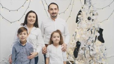 Sevgi dolu ebeveynler ve küçük çocuklar Noel ağacının yanında durup poz veriyorlar..