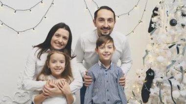 Komik bir videoda anne, baba ve kardeşler poz veriyor, dillerini gösteriyor ve yeni yılın ışıltılı arka planında surat asıyorlar..