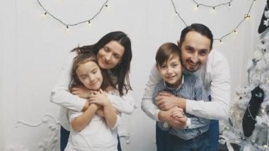 Mutlu aile üyeleri: Anne kucaklayan kızı, baba kucaklayan oğlu, Noel ağacının yanında beyaz arka planda..