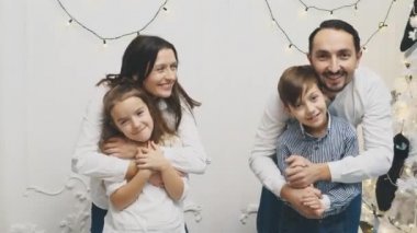 Mutlu aile üyeleri: Anne kucaklayan kızı, baba kucaklayan oğlu, Noel ağacının yanında beyaz arka planda..