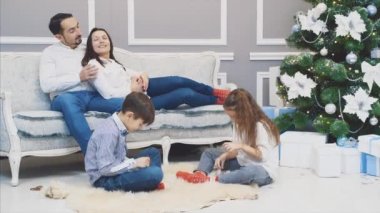 Sevgi dolu ebeveynler çocuklarına bakıyor, kar taneleri yetiştiriyor, kanepede oturuyor, konuşuyor ve gülümsüyor..