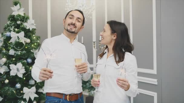 Romantic young couple share a toast clinking their glasses of white wine kissing and lightning bengal lights. — Stock Video