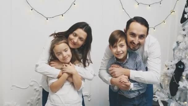 Happy family members: mother hugging daughter, father hugging son, on white background near christmas tree. — Stock Video