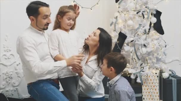 Madre, padre y hermano becalm pequeña hija llorando en el fondo blanco de Navidad . — Vídeo de stock