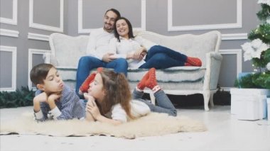 Komik erkek ve kız kardeş şakalaşıyor ve ön cephede suratlarını buruşturuyor, aileleri onlara bakarken, bulanık arka planda kanepede uzanıyorlar..