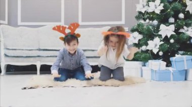 Noel geyiği boynuzu takan, önünde eğilen, gülümseyen ve komik görünen kardeşlerin komik videosu..